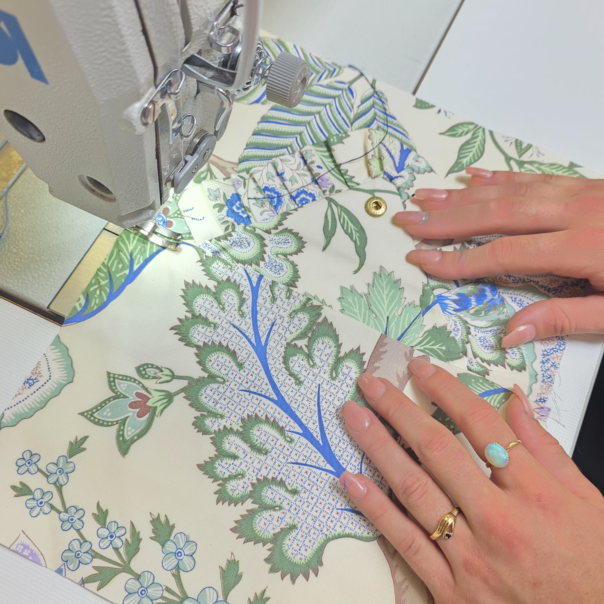 Mains cousant un tissu fleuri aux motifs bleus et verts dans un atelier de confection artisanale