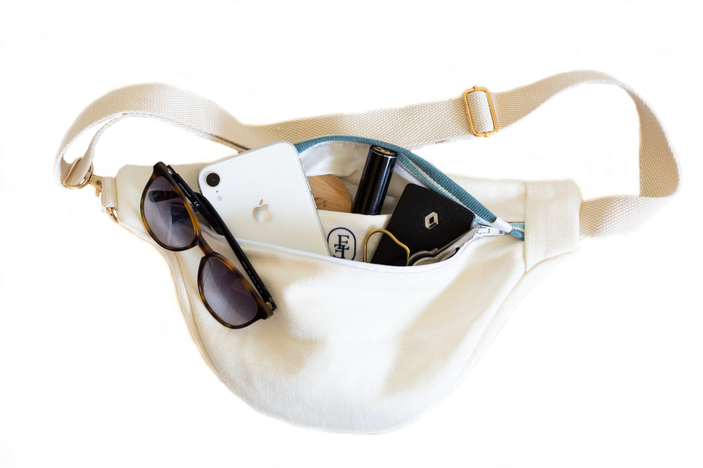 Banane écrue recyclée Étofé ouverte contenant des objets du quotidien : lunettes de soleil, téléphone, clés, rouge à lèvres et étiquette logo Étofé