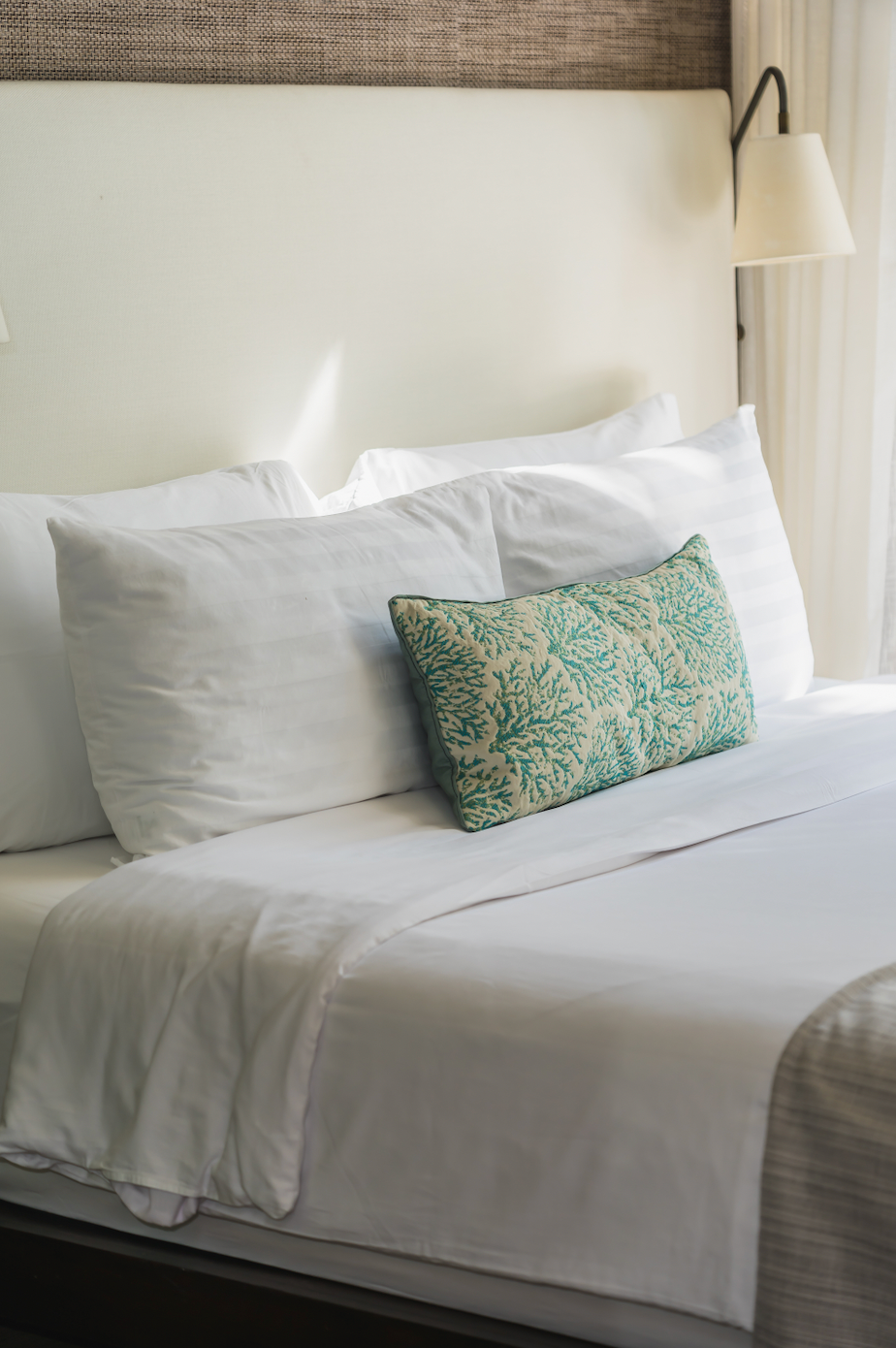 Lit d’hôtel soigneusement dressé avec coussin vert décoratif, parfait exemple de tissu d’ameublement pouvant être valorisé par ÉTOFÉ en accessoires uniques.
