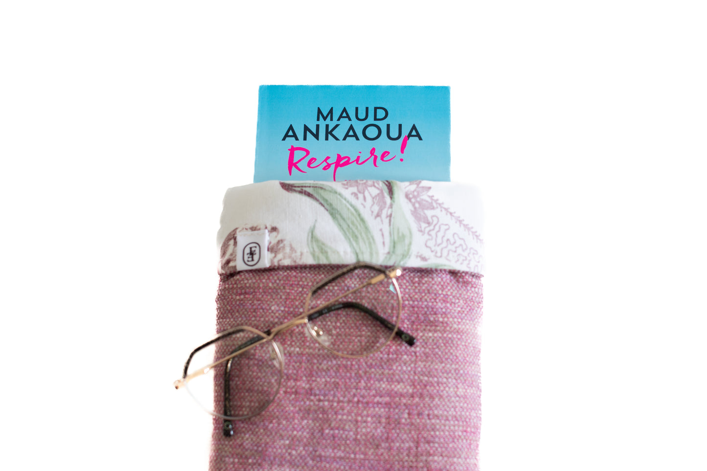 Housse ÉTOFÉ en tissu revalorisé rose avec rabat floral blanc et vert, contenant un livre bleu "Respire!" de Maud Ankaoua et une paire de lunettes posée devant. Accessoire éthique et fait main.