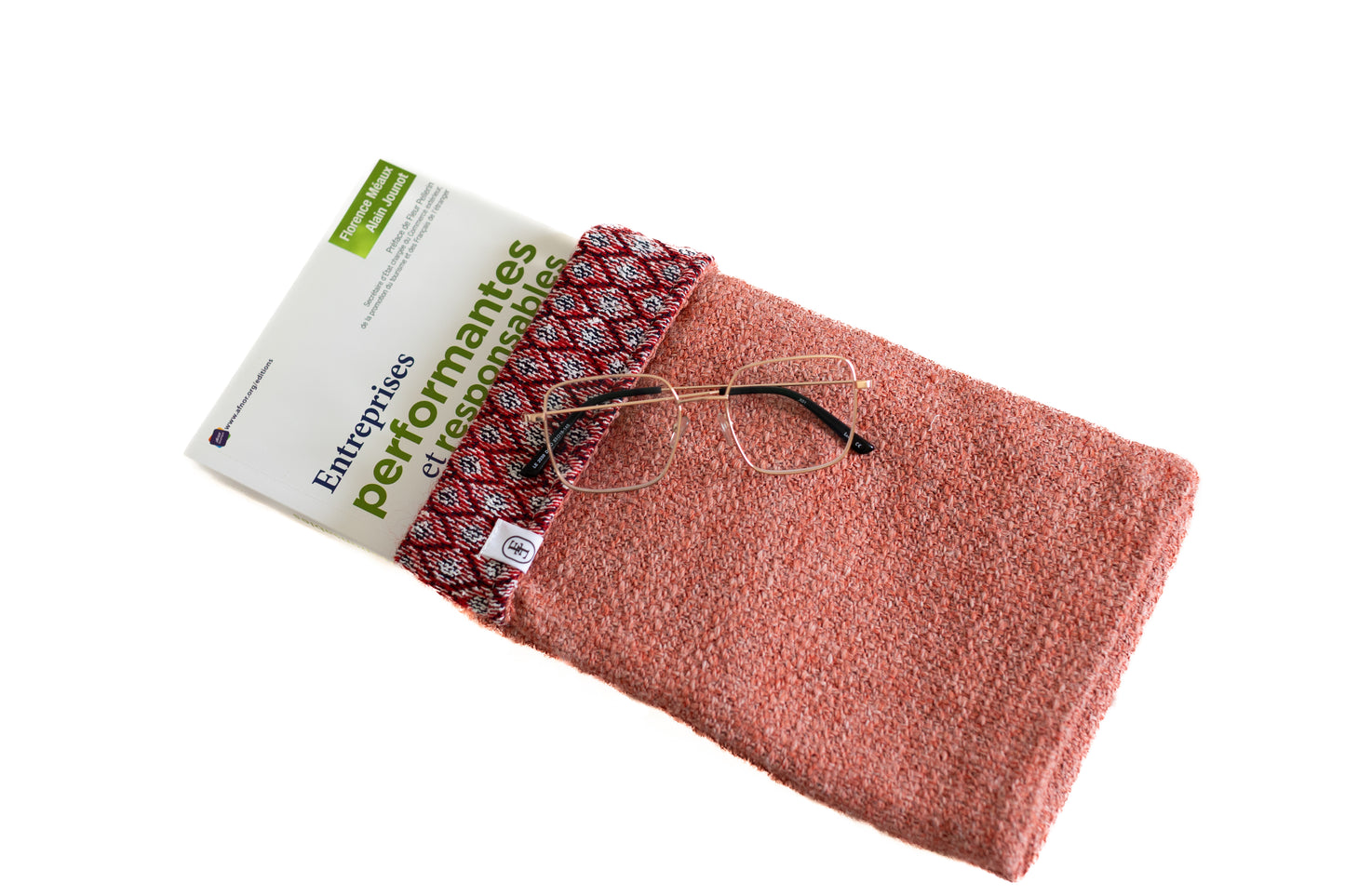 Housse ÉTOFÉ en tissu upcyclé terracotta avec motif graphique, contenant le livre Entreprises performantes et responsables et une paire de lunettes. Accessoire écoresponsable fabriqué à la main sur la Côte d’Azur.