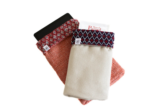Deux housses ÉTOFÉ en tissus revalorisés, l’une en rouge contenant une tablette, l’autre en beige avec rabat graphique abritant un livre de Marcel Pagnol. Accessoires faits main et durables, issus de l’upcycling textile.