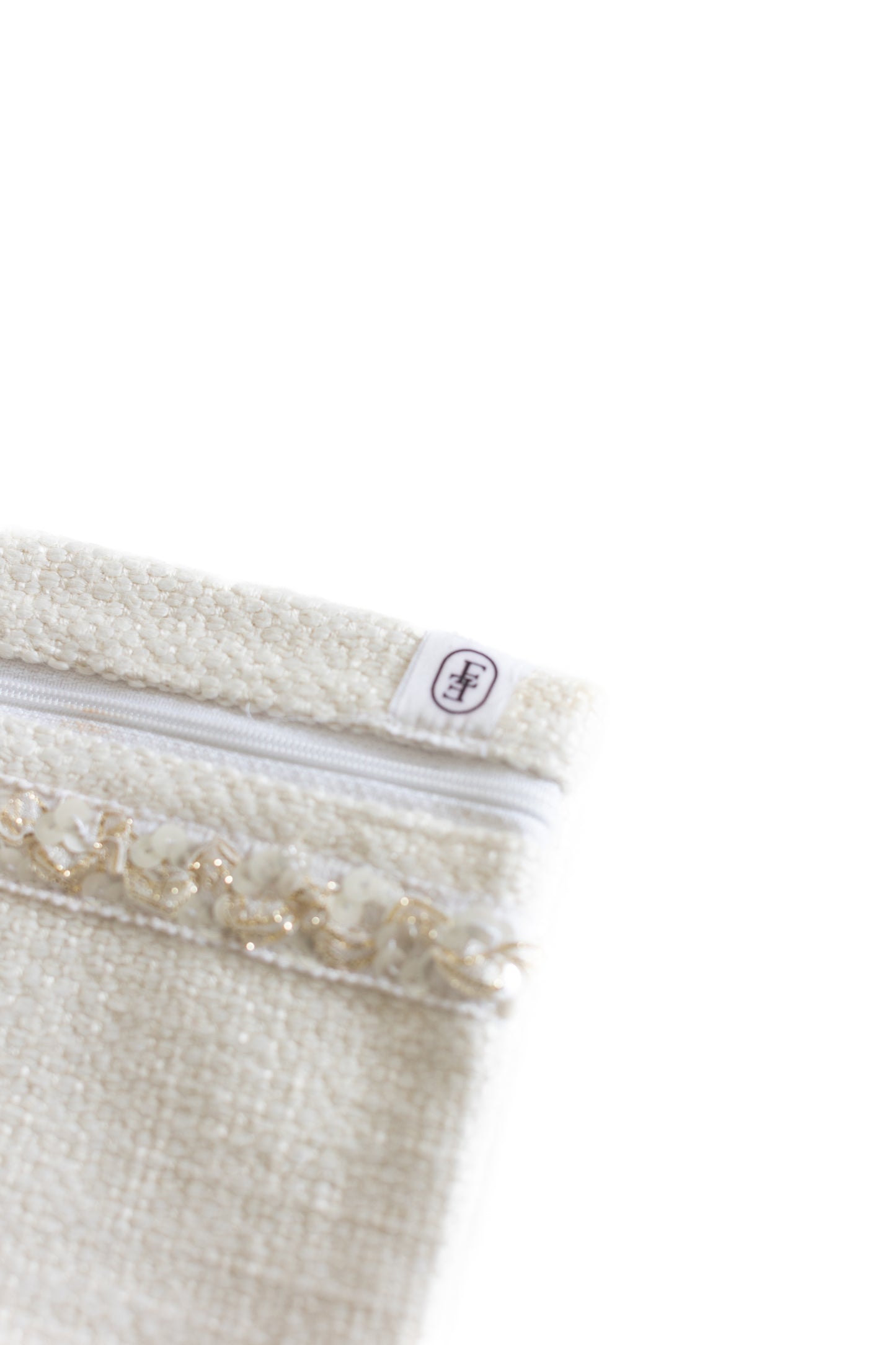 Détail de pochette plate ÉTOFÉ en tissu blanc bouclette avec fermeture blanche et galon doré, vue rapprochée du coin supérieur.