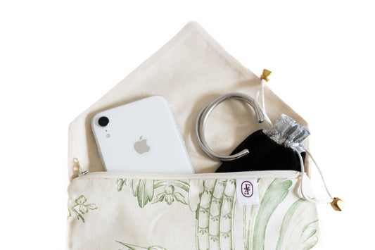 Zoom sur pochette ÉTOFÉ en tissu upcyclé, motif toile en jouy vert, contenant un iPhone et des accessoires argentés.