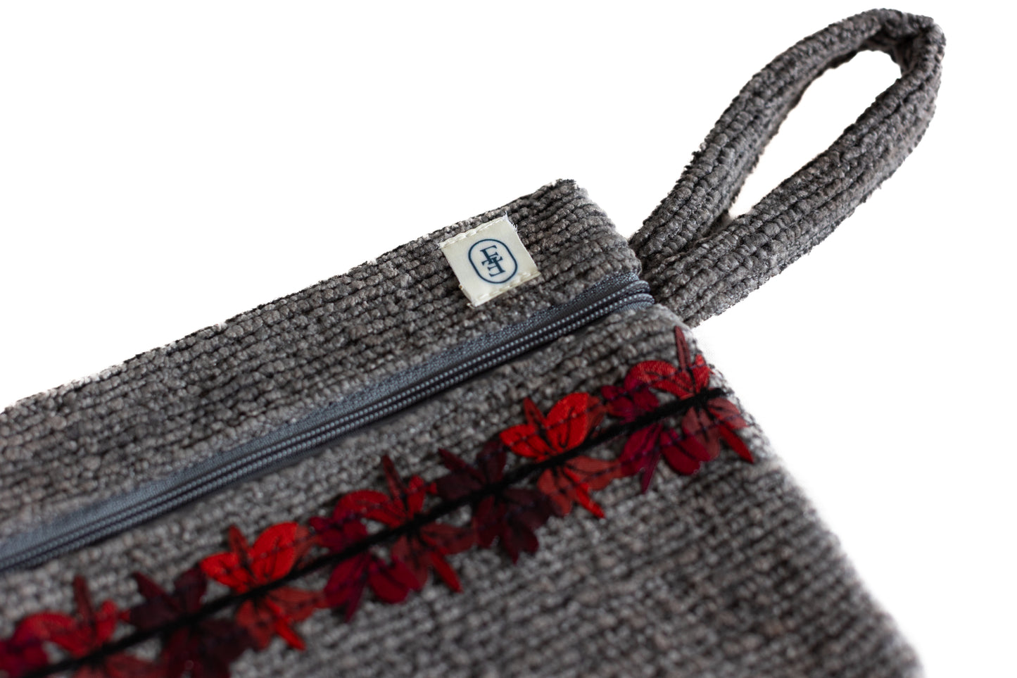 Pochette plate ÉTOFÉ grise en tissu texturé upcyclé, ornée d’un galon fleuri rouge et bordeaux, avec fermeture zippée et poignée assortie.