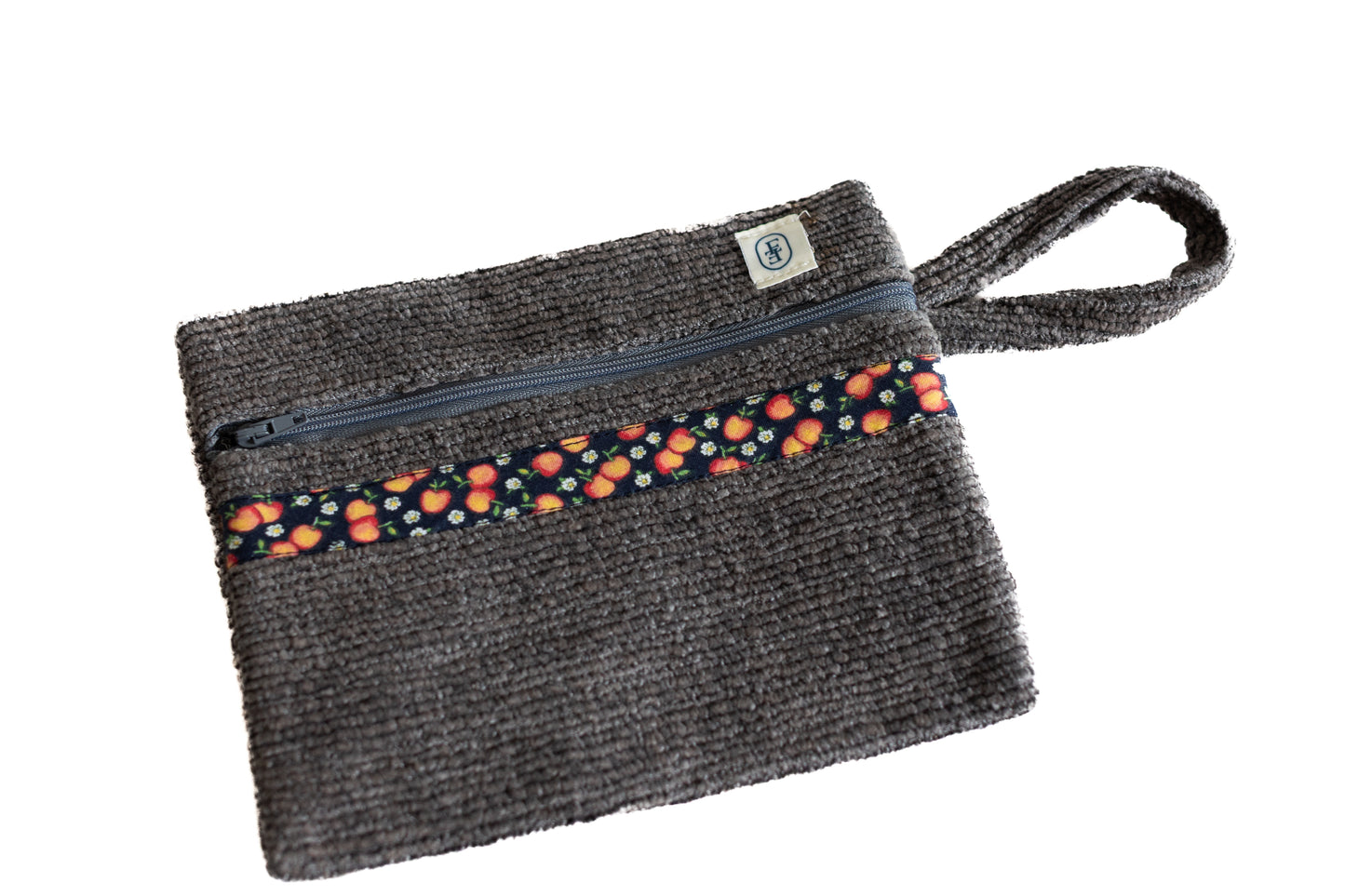 Pochette plate ÉTOFÉ en tissu bouclette grise, ornée d’un galon à motifs fruits colorés, avec fermeture zippée et poignée intégrée.