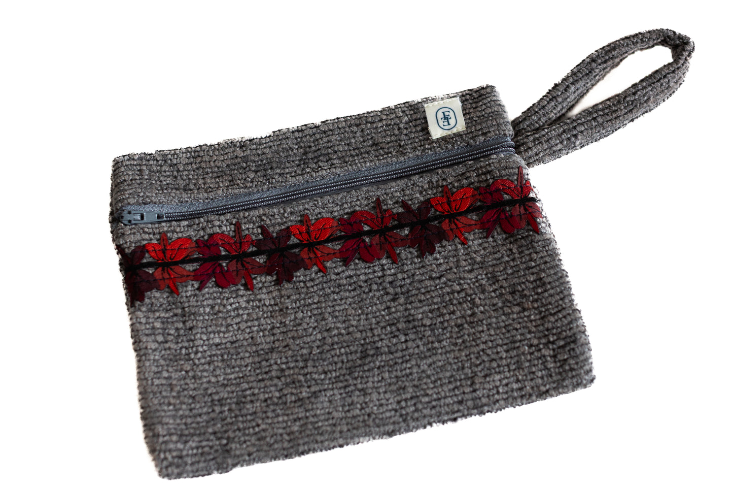 Pochette plate ÉTOFÉ grise en tissu bouclette, ornée d’un galon floral rouge et noir, avec fermeture zippée et poignée assortie.