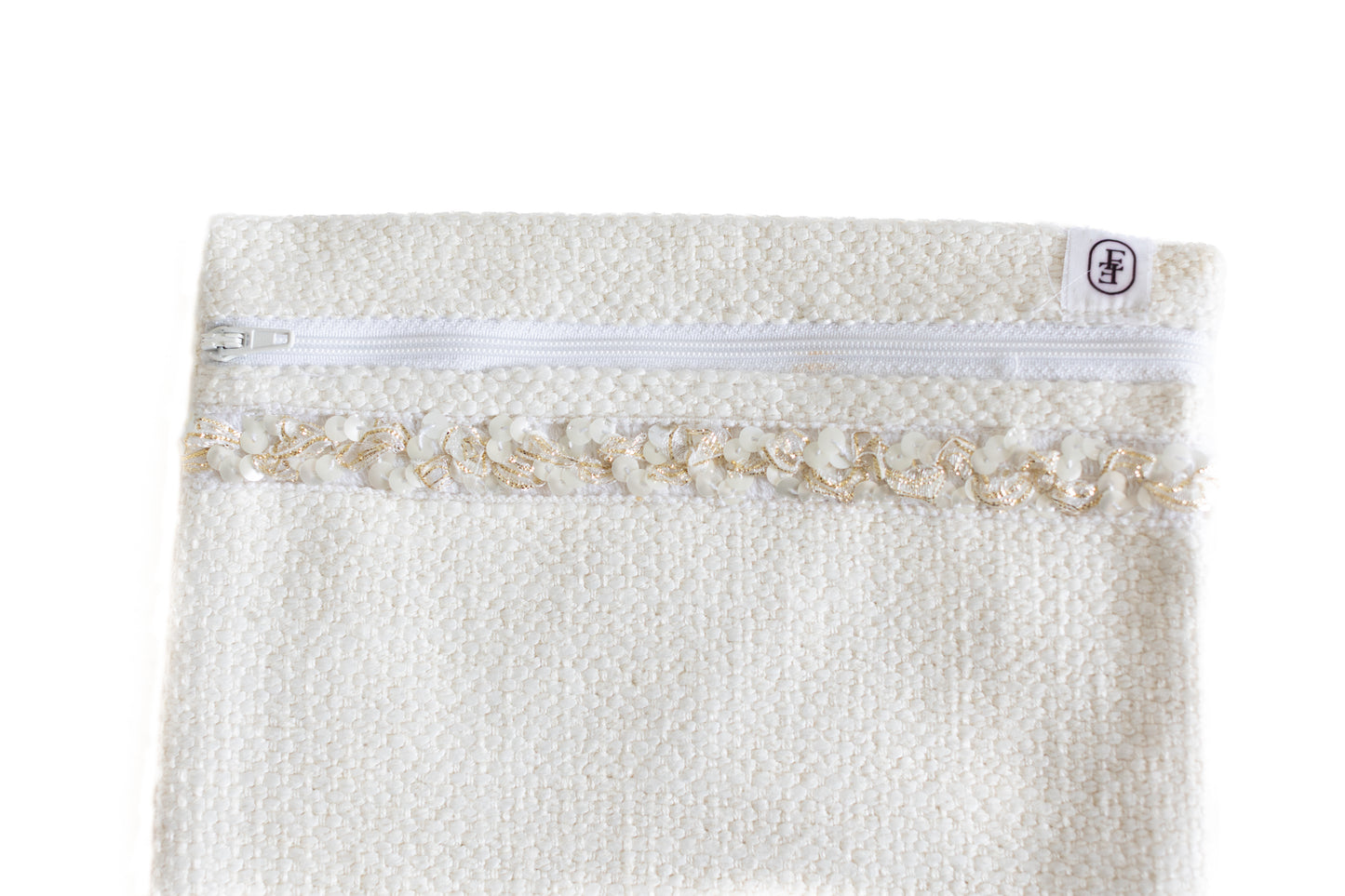 Gros plan sur pochette plate ÉTOFÉ blanche en tissu bouclette avec fermeture blanche et galon doré à volants.