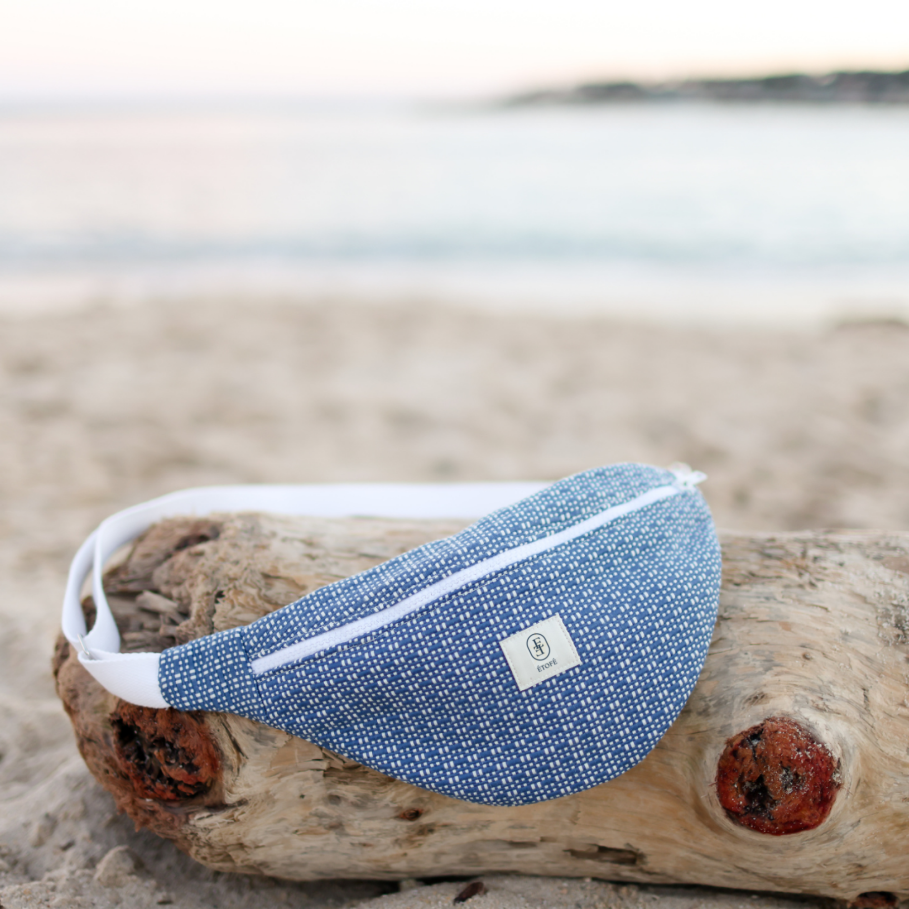 Sac banane ÉTOFÉ en tissu recyclé bleu, fait main sur la Côte d'Azur, posé sur une plage