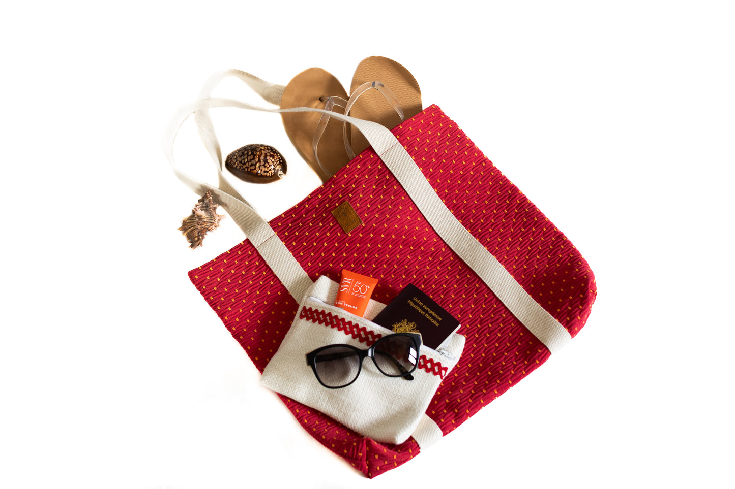 Sac cabas rouge en tissu recyclé avec accessoires d'été : lunettes, crème solaire, pochette blanche, passeport et sandales