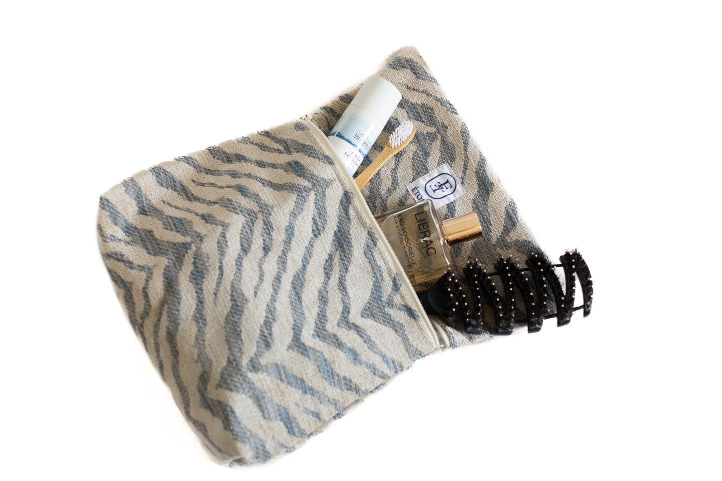 Trousse ÉTOFÉ en tissu recyclé zébré beige et bleu, ouverte avec accessoires de soin à l’intérieur – brosse à dents, spray, pince à cheveux.