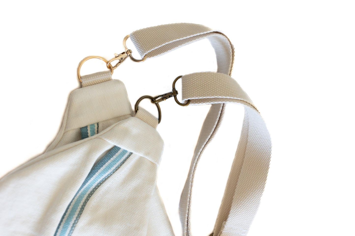 Gros plan sur la bandoulière ajustable et les attaches métalliques dorées d'une banane en tissu upcyclé crème, avec détail de la fermeture éclair bleu-vert.