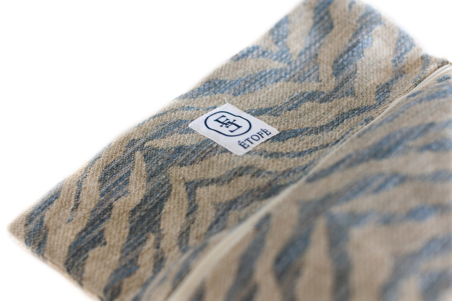 Gros plan sur le logo ÉTOFÉ cousu sur une trousse de toilette en tissu recyclé zébré beige et bleu – vue détaillée du textile.