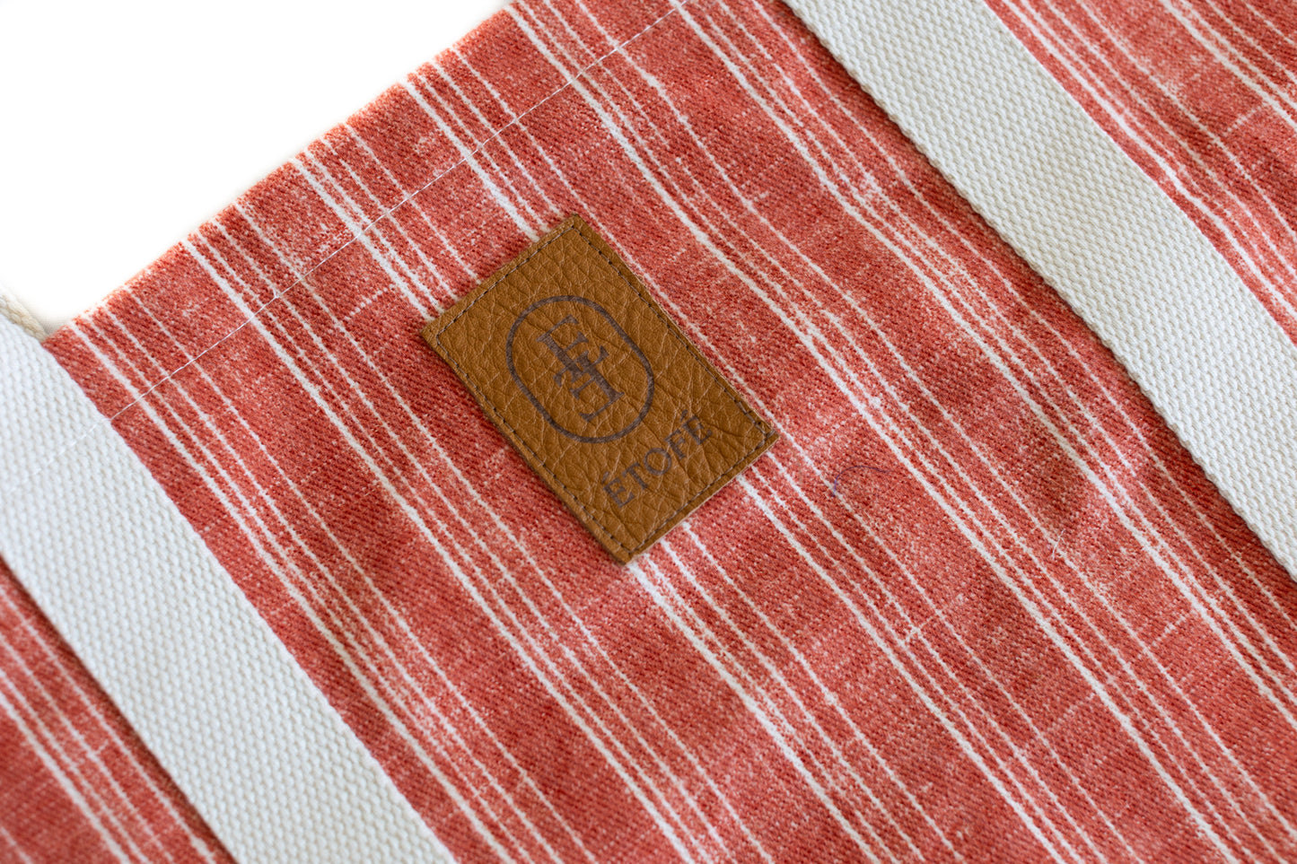 Zoom sur sac cabas ÉTOFÉ en tissu recyclé rouge à rayures, montrant le logo ÉTOFÉ en cuir cousu sur l'avant.