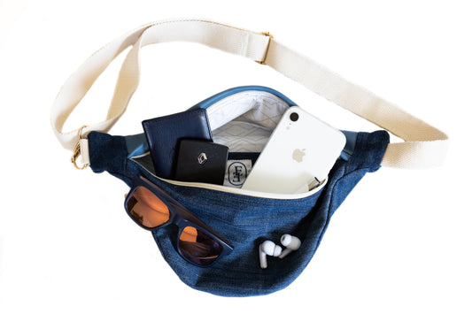 Banane en jean recyclé Étofé ouverte contenant un téléphone, des lunettes de soleil, des écouteurs sans fil et un porte-carte noir