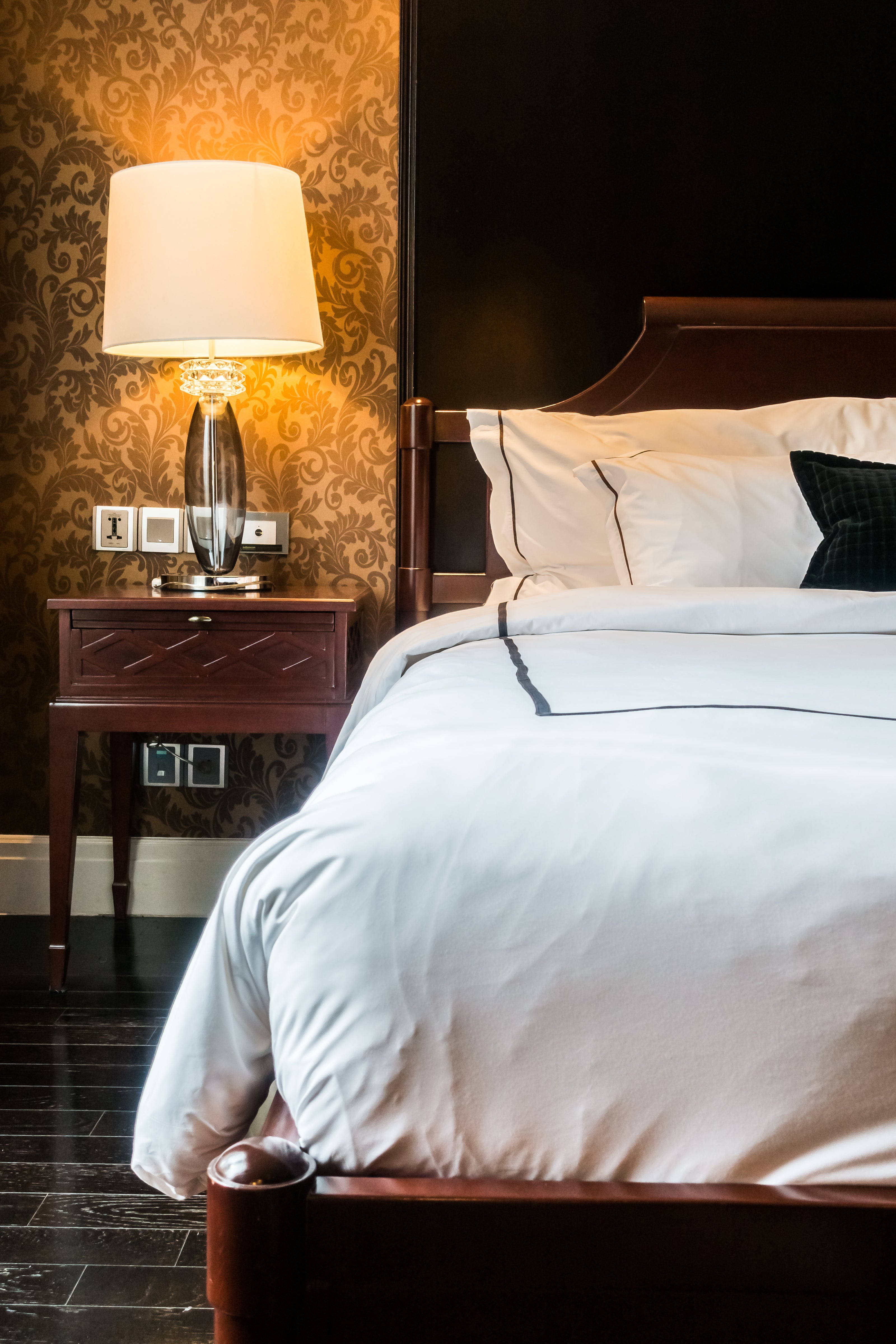 Chambre d’hôtel élégante avec tête de lit en bois, coussins décoratifs et lampe de chevet, illustrant des textiles haut de gamme propices à une seconde vie avec ÉTOFÉ.