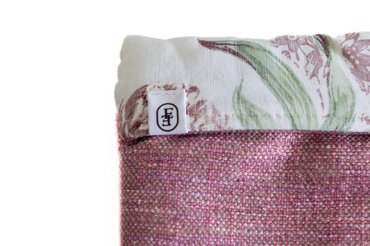 Détail d’une housse ÉTOFÉ en tissu revalorisé, avec logo cousu sur une bordure fleurie et corps en matière rose texturée. Accessoire fabriqué à la main en circuit court sur la Côte d’Azur.