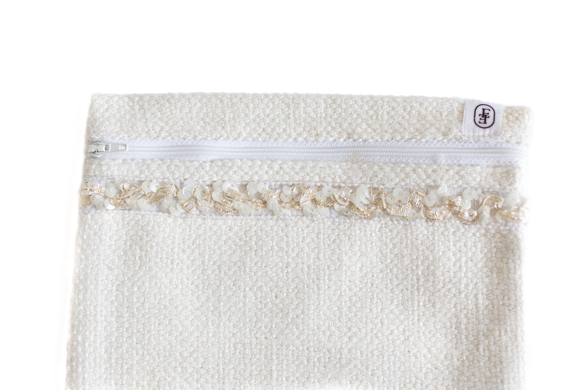 Gros plan sur pochette plate ÉTOFÉ blanche en tissu bouclette avec fermeture blanche et galon doré à volants.