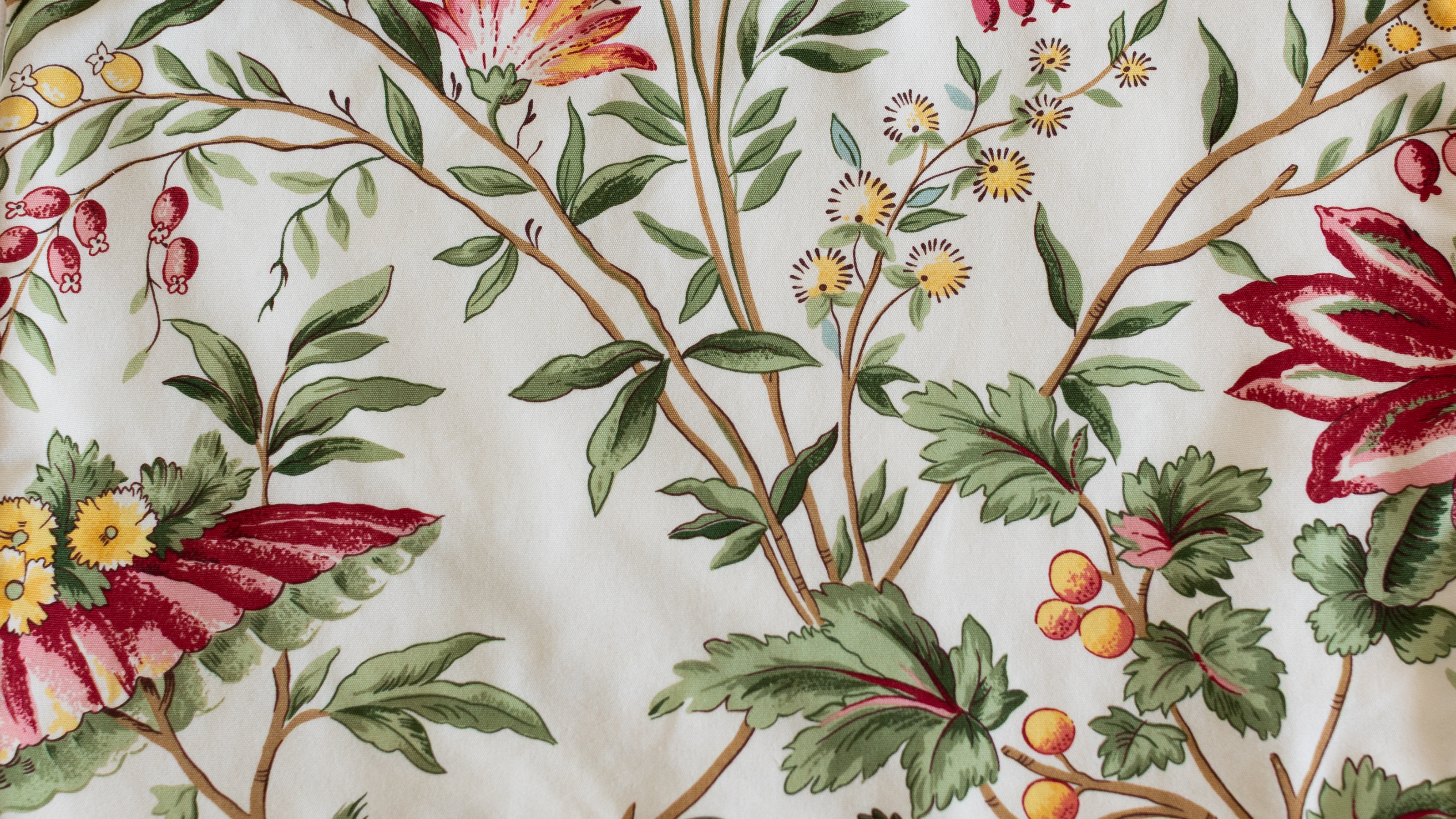 Motif fleuri botanique ancien sur tissu blanc avec feuillages verts, fleurs rouges et jaunes, utilisé dans les créations artisanales ÉTOFÉ.