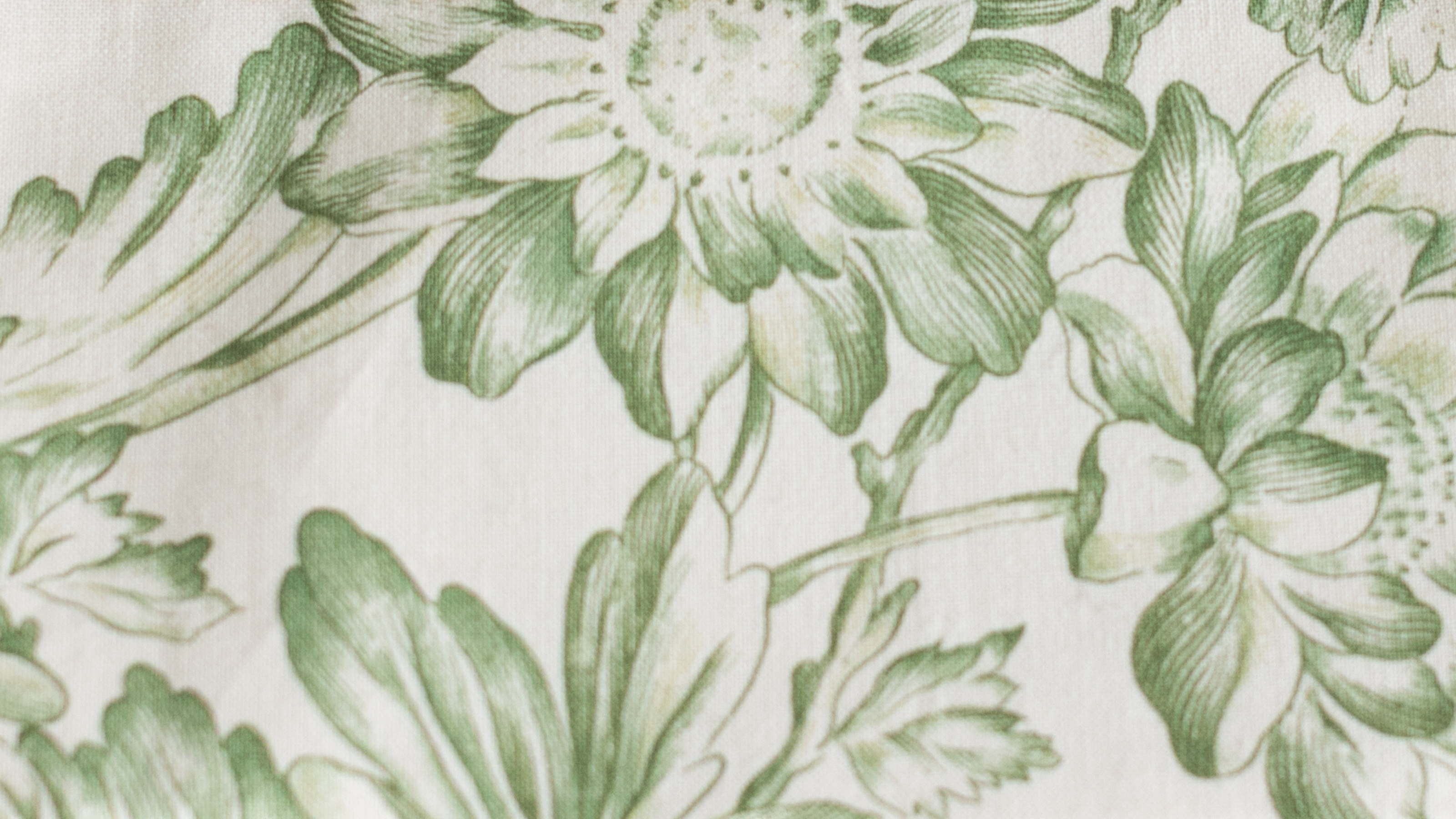 Gros plan sur un tissu ancien imprimé de grandes fleurs vertes stylisées sur fond crème. Motif végétal vintage utilisé dans la confection artisanale des pochettes ÉTOFÉ.