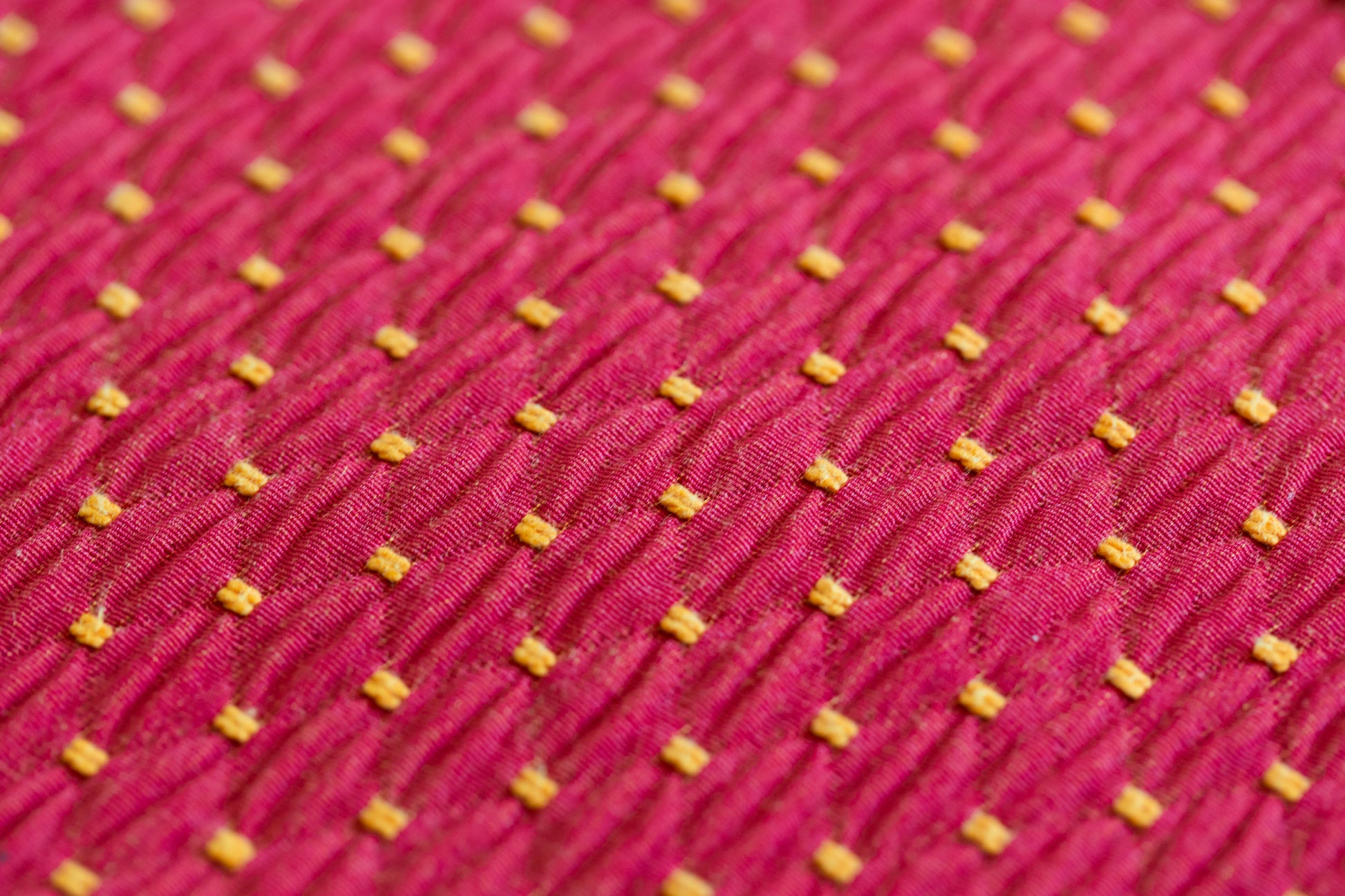 Gros plan sur un tissu rouge à motifs jaunes utilisé pour les sacs ÉTOFÉ, illustrant le détail du tissage et la qualité du tissu recyclé.