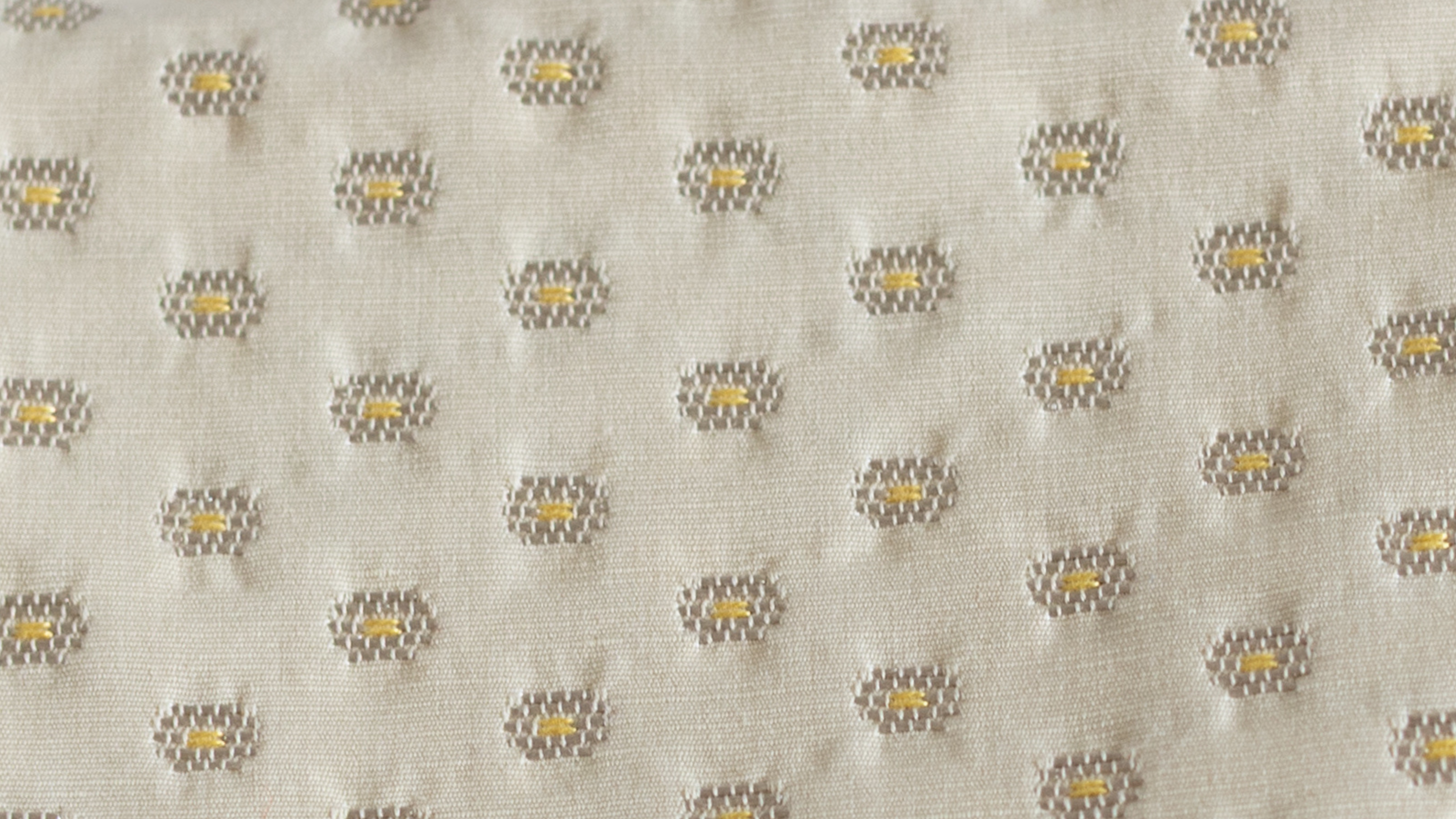 Gros plan sur un tissu écru brodé de petits motifs floraux jaunes et gris, utilisé pour les créations artisanales de la marque ÉTOFÉ.