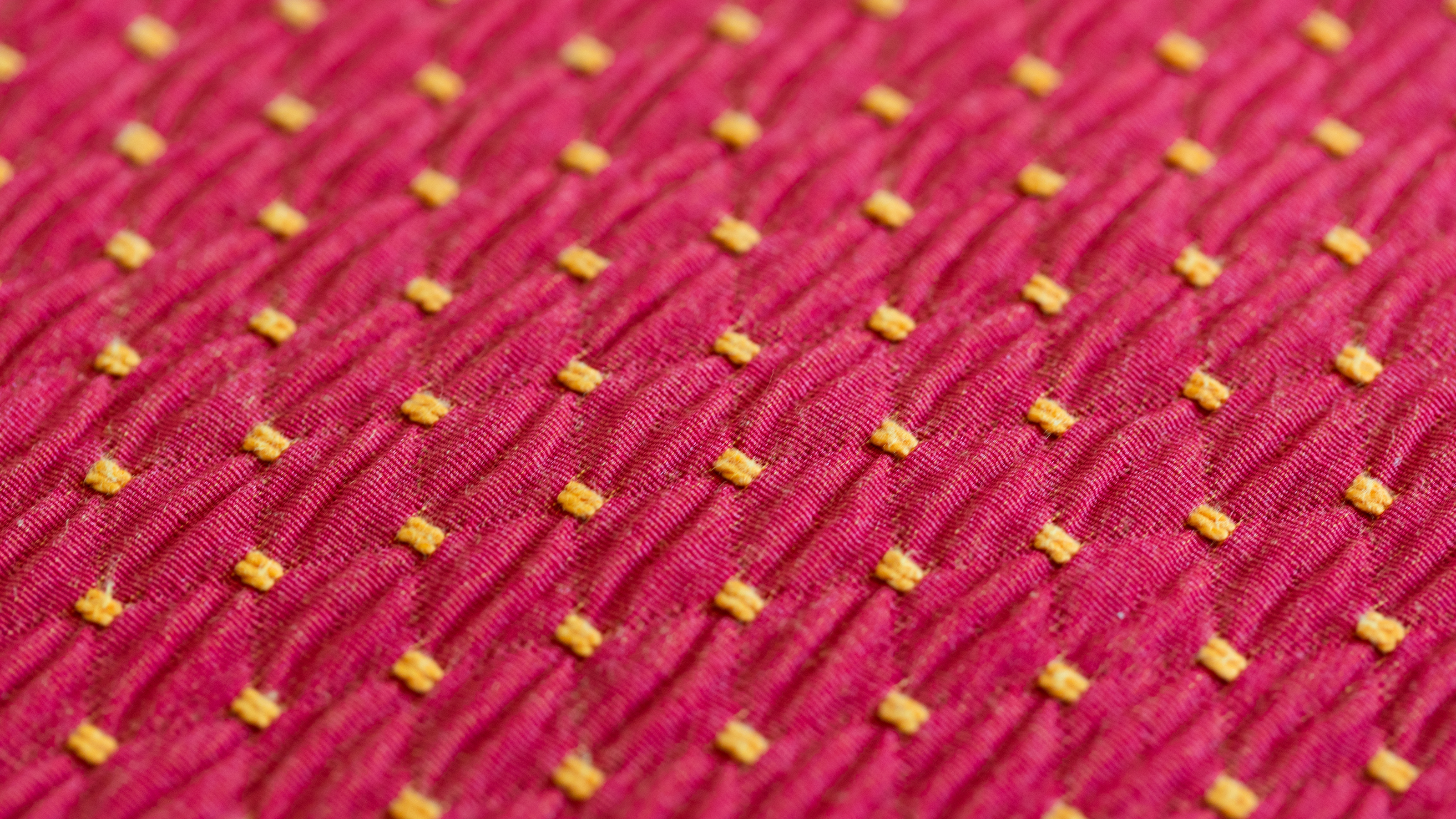 Gros plan sur un tissu rose texturé orné de petits carrés brodés jaunes, utilisé dans les créations textiles artisanales de la marque ÉTOFÉ